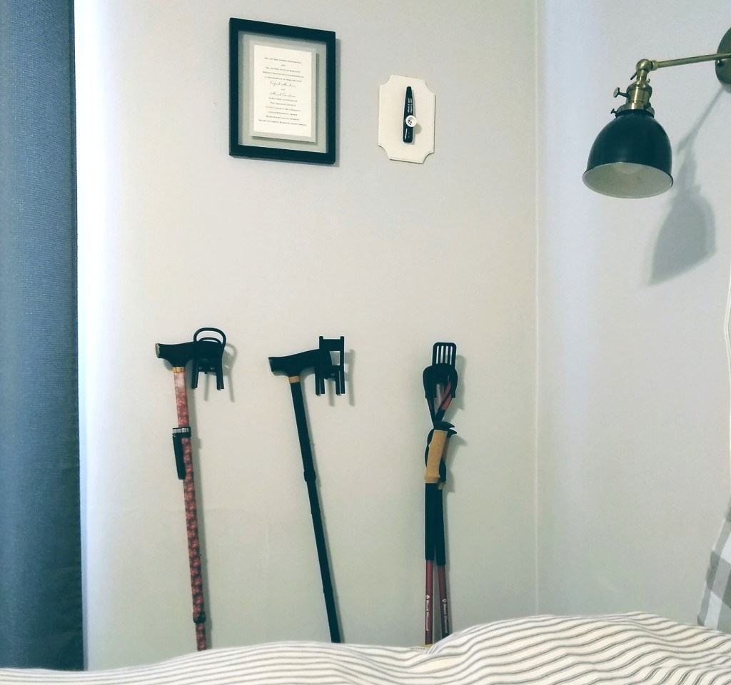 Image shows a wall with three chair-shaped wall hooks holding canes and walking sticks. 
