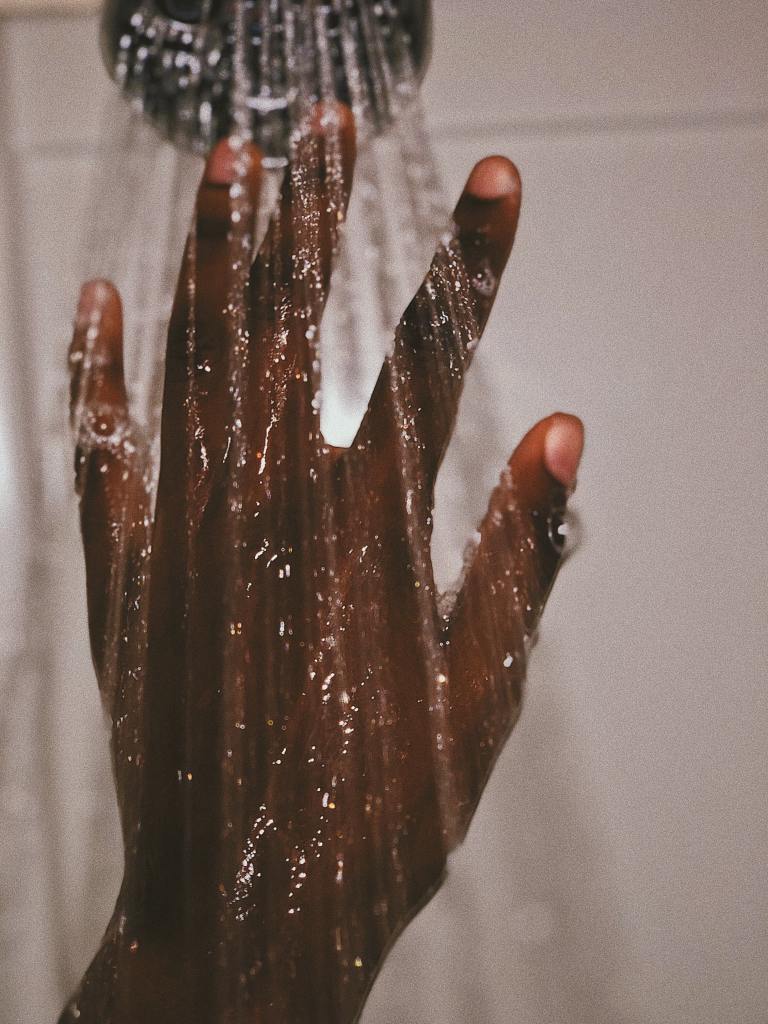 Image of male African American hand under shower water. 