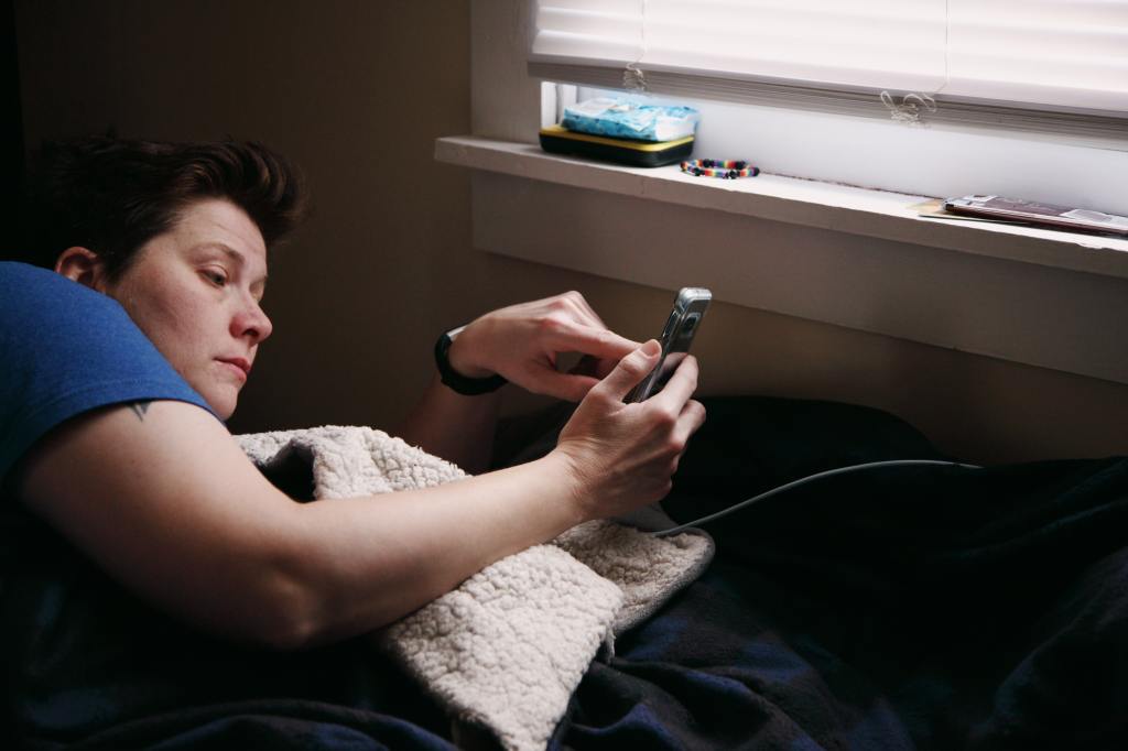 Image of Caucasian woman in bed looking at smartphone.