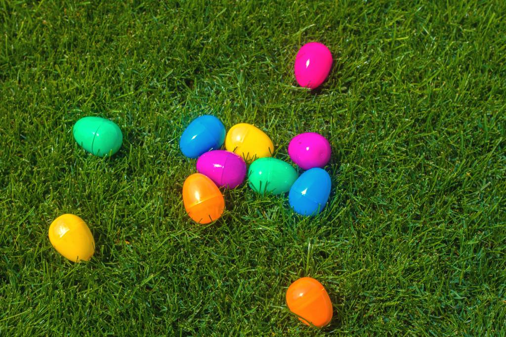 Multicolored plastic Easter eggs scattered on green grass. 