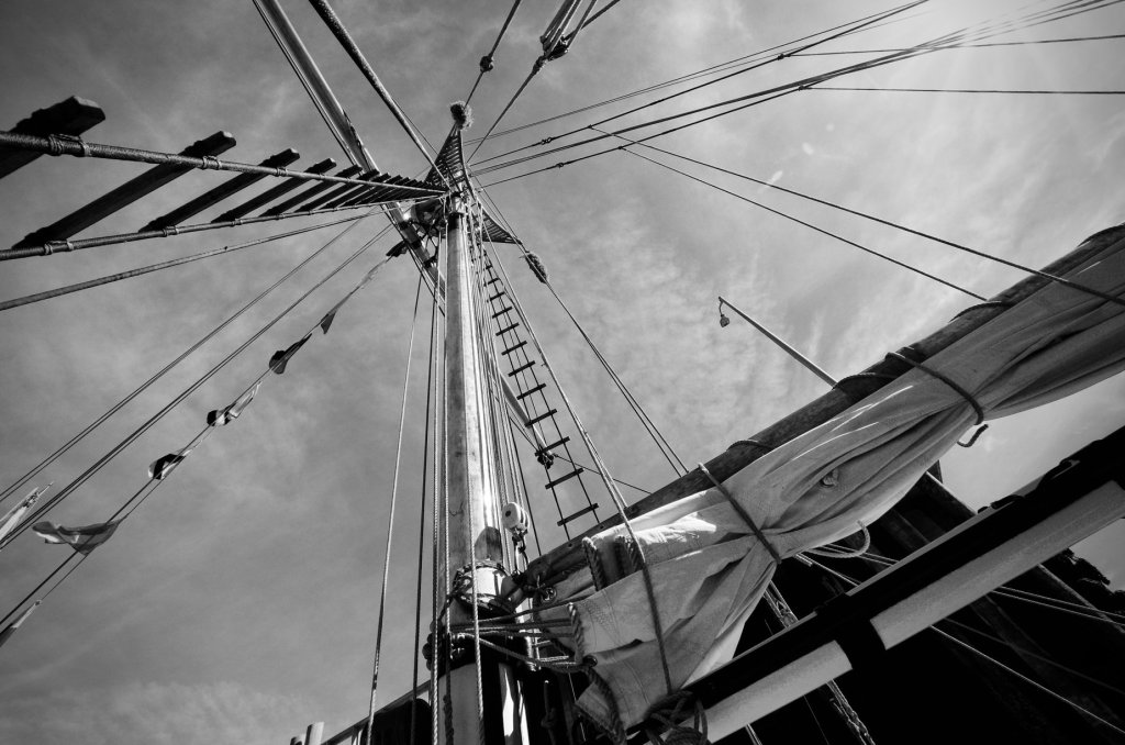 Black and white image looking upward along a ship mast, with rigging and sails visible. 