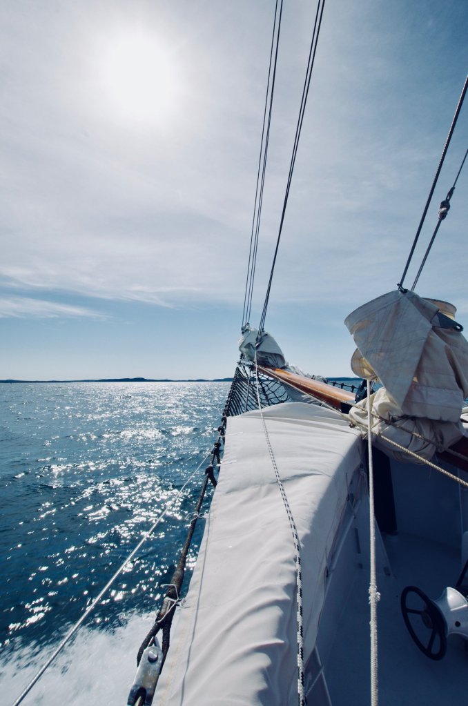 Bow of a sailboat is seen against the sparkling sea, with link to Jolly Breeze site.