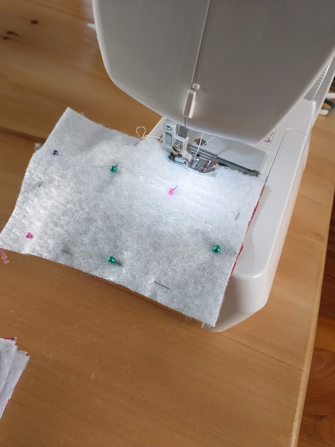 The fabric pieces are shown pinned around the edges, set under the presser foot of a sewing machine.