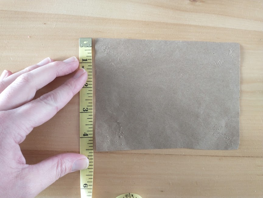 A rectangular piece of brown kraft paper, with a hand holding a measuring tape to the left edge, measuring 4 1/2 inches.
