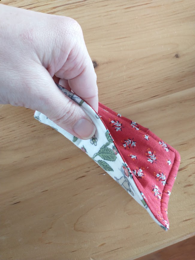 A hand is lifts the sponge so that both sides are visible, as well as the finished seam along the top edge.