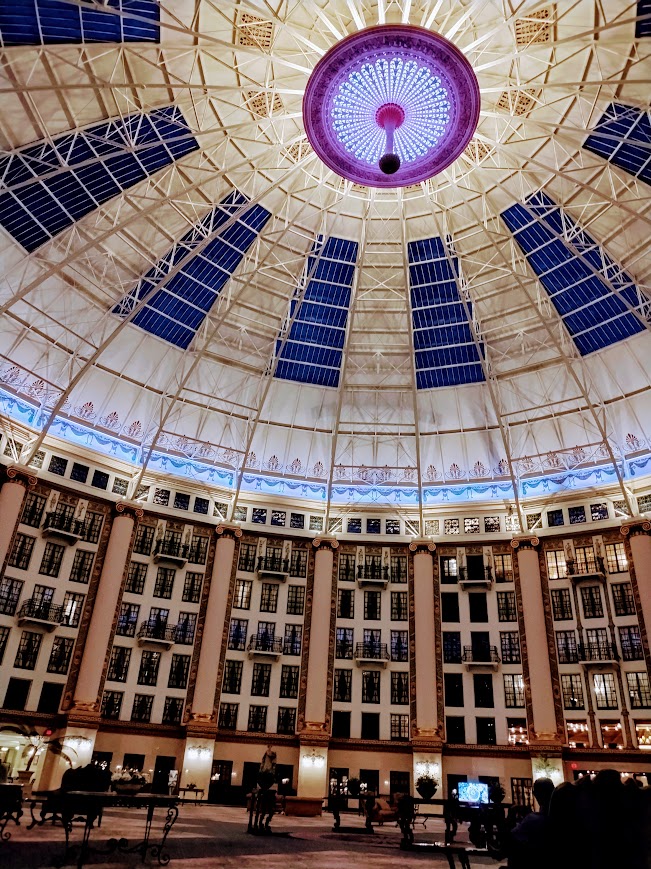The same atrium, dark at night, with the dome lit up with blue and purple lighting.