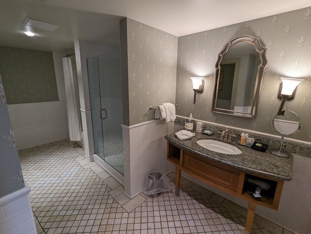 A spacious bathroom with wide vanity, large walk-in shower, and bathtub. An adjacent wall holds a small room with toilet.