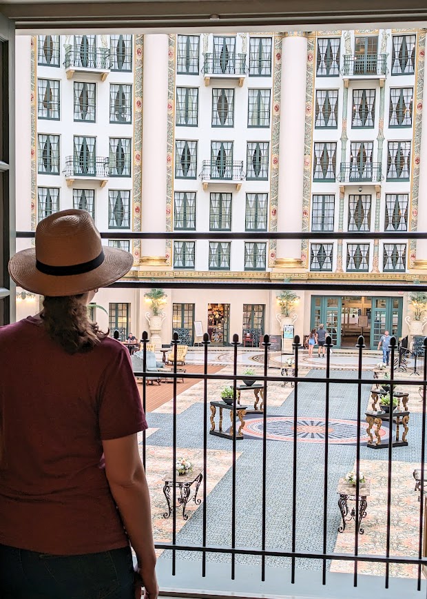 The author in a fedora looks out on the atrium from an upper window with metal grating.